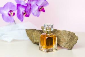 A perfume bottle stands on a stone against a background of beautiful orchids. Stylish appearance, layout, personality. Banner, a place for the text. photo