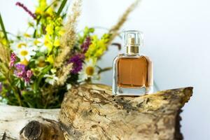 a perfume bottle on the background of a dry stump, tree bark and a bouquet of wild flowers. Stylish appearance, layout, personality. Banner, a place for the text. photo