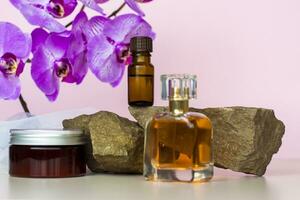 A cosmetic product and a perfume bottle stand on a stone against a background of beautiful orchids. Stylish appearance, layout, personality. Banner, a place for the text. photo