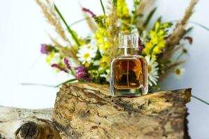 a perfume bottle on the background of a dry stump, tree bark and a bouquet of wild flowers. Stylish appearance, layout, personality. Banner, a place for the text. photo