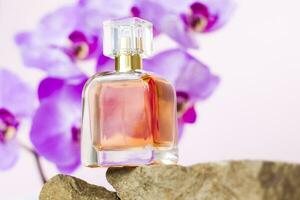 A perfume bottle stands on a stone against a background of beautiful orchids. Stylish appearance, layout, personality. Banner, a place for the text. photo