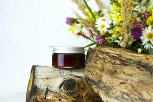 a jar of cream on the background of a dry stump, tree bark and a bouquet of wild flowers. Stylish appearance, layout, personality. Banner, a place for the text. photo