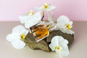 A perfume bottle stands on a stone against a background of beautiful orchids. Stylish appearance, layout, personality. Banner, a place for the text. photo