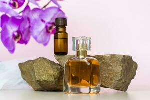 A cosmetic product and a perfume bottle stand on a stone against a background of beautiful orchids. Stylish appearance, layout, personality. Banner, a place for the text. photo