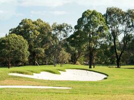 Golf Course with Green Grass and small Sand Pit, area of land laid out for golf putting green and often one or more natural or artificial hazards. photo