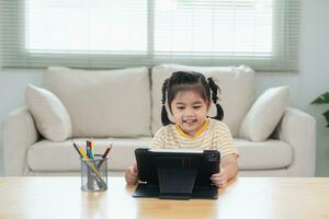 Asian girl looking and touch on white screen at the tablet screen attentively. overstimulated children concept. Too much screen time. Cute girl watching videos while tv, Internet addiction concept. photo