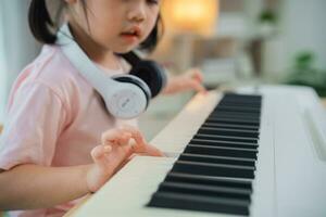 cerca arriba. asiático linda niña sonrisa vistiendo blanco auricular jugando aprendizaje en línea piano música en vivo habitación a hogar. el idea de ocupaciones para niño a hogar durante cuarentena. música aprendizaje estudiar. foto