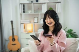 Woman using mobile phone smartphone holding credit card to shopping online. asian woman working at home. Online shopping, e-commerce, internet banking, spending money, working from home concept. photo