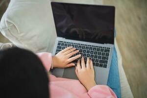 Top view. Asian freelance woman smile lying relax and typing on keyboard and working on laptop on sofa couch. Entrepreneur woman working for business at living room home. Business work home concept. photo