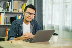 Smart Asian man smiling wearing glasses working with computer laptop. concept work form home, stay at home. freelance life style, New normal social distancing lifestyle. Work form anywhere concept. photo