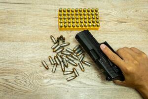 Male hand holding a pistol, bullets and mags on a wooden table. photo