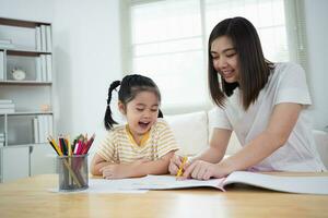 Cute little child painting with colorful paints. Asian girl and mother using crayon drawing color. Daughter and mom doing homework coloring cartoon characters. Baby artist activity lifestyle concept. photo