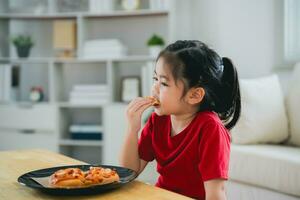 asiático contento niños niña comiendo Pizza y sonriente en el vivo habitación a hogar. niños niña comiendo y saboreo italiano hecho en casa Pizza en casa. foto