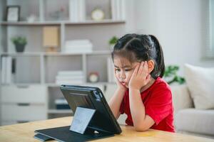 Asian child girl serious to looking using and touch tablet display screen. Baby smiling funny time to use tablet. Too much screen time. Cute girl watching videos while tv, Internet addiction concept. photo