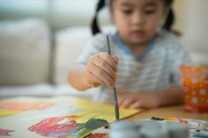 Close up hand of cute little asian baby smiling painting with colorful paints using watercolor. Asian girl using paintbrush drawing color. Baby activity lifestyle concept. photo