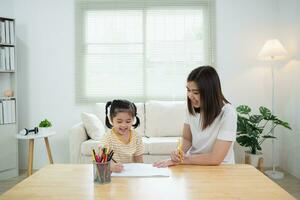 Cute little child painting with colorful paints. Asian girl and mother using crayon drawing color. Daughter and mom doing homework coloring cartoon characters. Baby artist activity lifestyle concept. photo