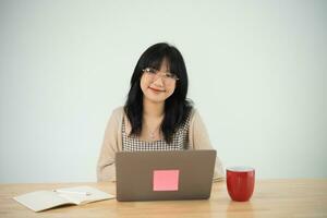 Asian freelance woman wearing glasses typing on keyboard and working on laptop on wooden table at home. Entrepreneur woman working for her business at living room home. Business work home concept. photo