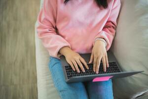 parte superior vista. asiático Lanza libre mujer sonrisa acostado relajarse y mecanografía en teclado y trabajando en ordenador portátil en sofá sofá. empresario mujer trabajando para negocio a vivo habitación hogar. negocio trabajo hogar concepto. foto