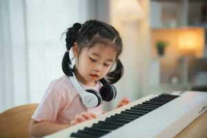 asiático linda niña sonrisa y vistiendo blanco auricular jugando aprendizaje en línea piano música en el vivo habitación a hogar. el idea de ocupaciones para el niño a hogar durante cuarentena. música aprendizaje estudiar. foto