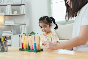 Young cute Asian girl and her parent mother mom is learning the abacus with colored beads to learn how to count sofa in the living room at home. Child baby girl development studing concept. photo