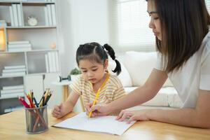 lindo niño pequeño pintando con pinturas de colores. niña asiática y madre usando color de dibujo de crayón. hija y mamá haciendo la tarea coloreando personajes de dibujos animados. concepto de estilo de vida de actividad de artista bebé. foto