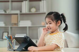 Asian girl looking and touch on white screen at the tablet screen attentively. overstimulated children concept. Too much screen time. Cute girl watching videos while tv, Internet addiction concept. photo