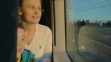 Small boy with mother sitting against window in their rail train place and watching outside video