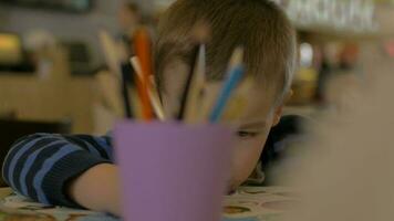 pequeño chico resuelve niños ejercicio en desarrollando libro para preescolar niños desenfocado vaso con lapices en el primer plano video