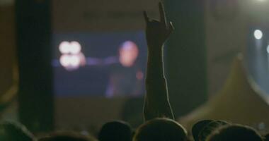 toeschouwer Mens tonen een steen, duivel hoorns gebaar in voorkant van groot scherm Bij buitenshuis muziek- concert video