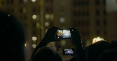 View from behind of hands hold smartphone among people at rave party with light video