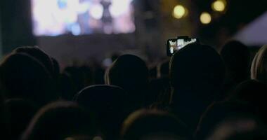 View from behind of hands hold camera with digital display among people at rave party with light video