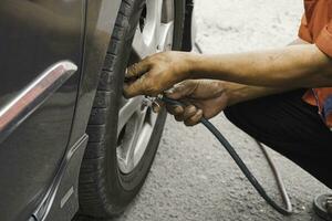 man driver hand inflating tires of vehicle, removing tire valve nitrogen cap for checking air pressure and filling air on car wheel at gas station. photo