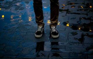 en pie Delgado joven del hombre piernas reflejado en bulboso, circular bokeh de agua de lluvia atrapado en el cemento piso. en el solitario noche foto