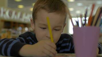 en la mesa sentado un niño pequeño y dibuja con lápices de colores video