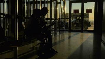 beim Flughafen von Thessaloniki, Griechenland im das warten Zimmer sitzt ein Mutter mit ihr Sohn und Aufpassen Videos auf Tablette