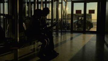 At airport of Thessaloniki, Greece in the waiting room sits a mother with her son and watching videos on tablet