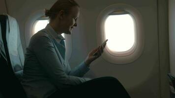 In cabin of plane girl sitting on chair and using mobile terminal on phone and pays for purchase through card video
