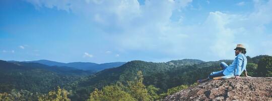 Asian man travel relax in the holiday. seats relax read books on rocky cliffs. On the Moutain summer. In Thailand photo