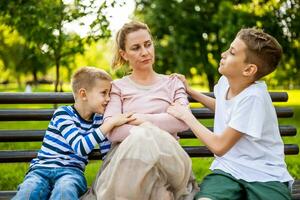 Mother is sitting with her sons on bench in park. She is angry and the boys try to apologize. photo