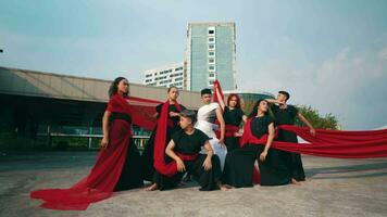 a group of Asian men stood and posed with red veils tied around their bodies in front of a magnificent building video