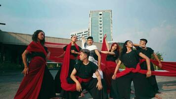 a group of Asian men stood and posed with red veils tied around their bodies in front of a magnificent building video