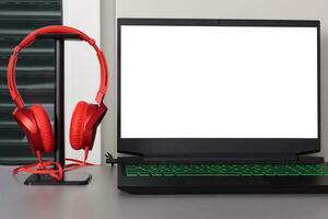 Gray Desk Setup with Laptop and Red Headphones. Blank white screen. photo