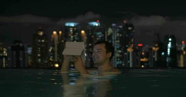 Man with pad in rooftop pool of night Kuala Lumpur video