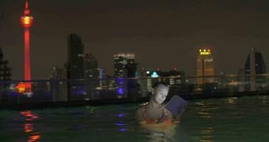 In pool on roof of a hotel in Kuala Lumpur, Malaysia is swimming young girl and works on tablet video