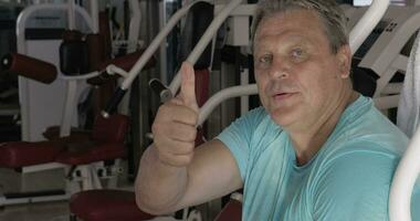 Sénior homme avec pouce en haut et sourire entre des exercices dans Gym video