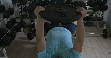 Grown man in a gym lying on bench and raises damn over head video