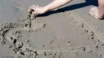 Kinder- Hände spielen im das Sand mit Ihre Hände zu zeichnen ein Herz gestalten auf das Strand. video