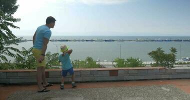 Young man and son are throwing rocks against boats harbor in sea Piraeus, Greece video