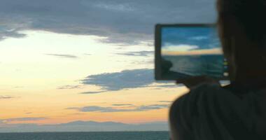 kvinna tar foton av de skön landskap av de hav och kväll himmel med henne läsplatta på solnedgång video