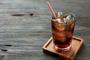 A Glass of Cola with Ice on Wooden Table photo